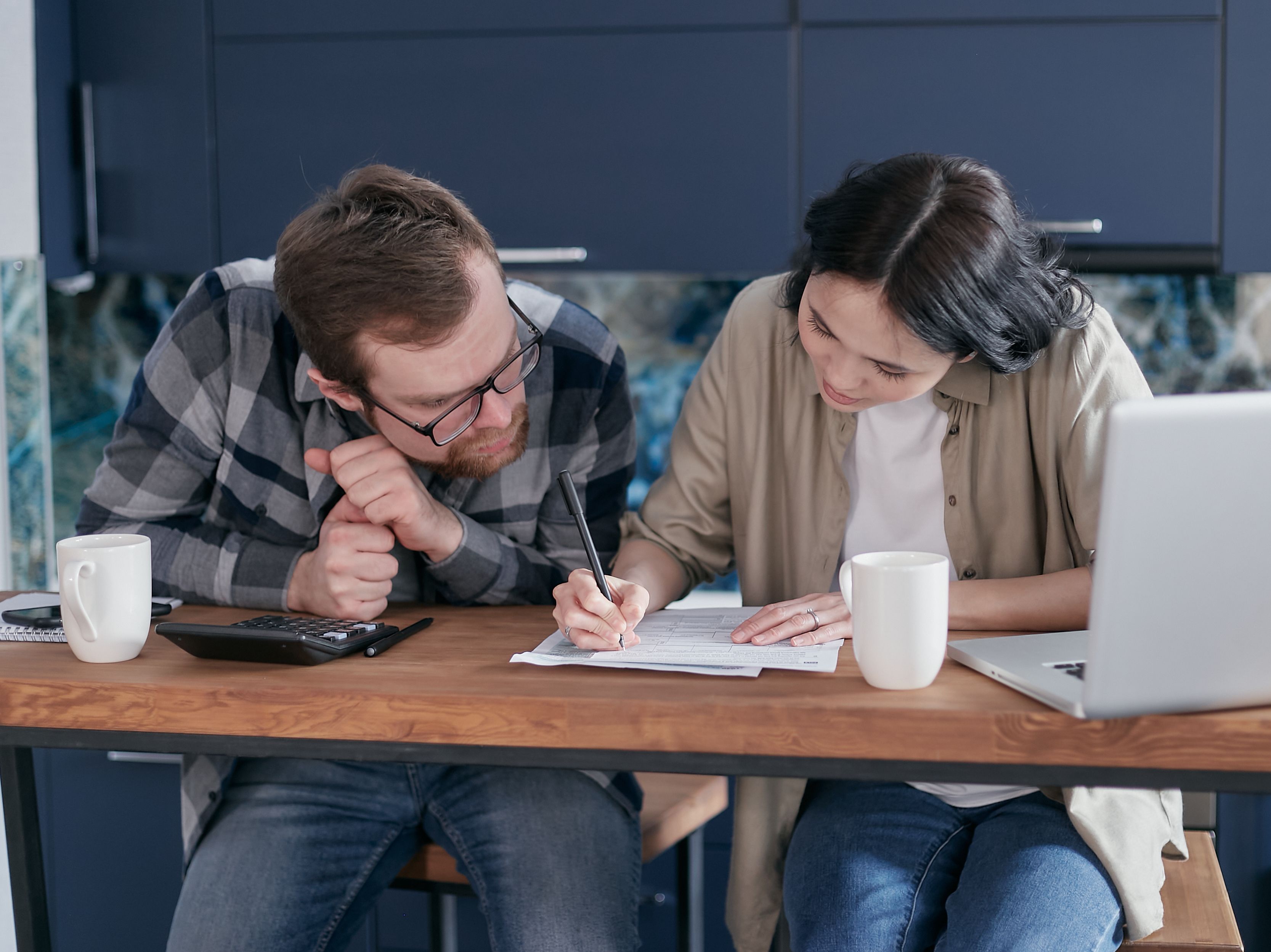 Casal revisando orçamento familiar juntos, com calculadora, papéis e notebook sobre a mesa